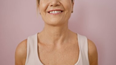 Sarı saçlı, gülümseyen orta yaşlı bir kadın pembe izole edilmiş arka planda pozitiflik tasvir ediyor..