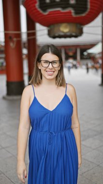 Gülümseyen ve neşeli, gözlüklü güzel İspanyol kadın Tokyo 'daki sembolik senso ji türbesine özgüvenle poz veriyor, doğal güzellik ve kaygısız mutluluk yayıyor.