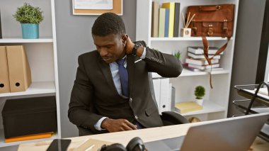 Takım elbiseli yakışıklı bir Afrikalı modern ofis ortamında çalışırken boynu ağrıyor..