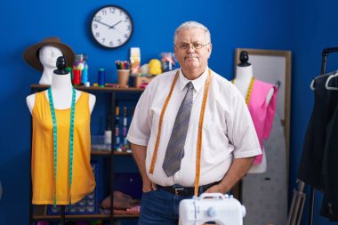 Orta yaşlı, gri saçlı, terzi dükkanında kendine güvenen bir terzi.