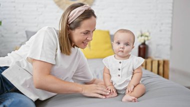 Kendine güvenen anne ve kız çocuğu, mutlu bir anı paylaşıyorlar, rahat bir yatak odasında birlikte oturuyorlar, sevgi ve mutluluğun tadını çıkarıyorlar. Gülümseyen yüzleri odada olumlu bir hava yayıyordu..