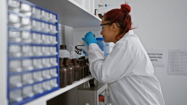 Ateşli genç kızıl saçlı bilim kadını tıbbi araştırmalara daldı, yoğun laboratuarda mikroskopla çalışıyor.