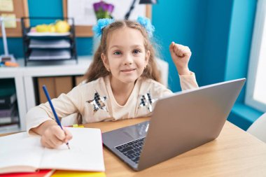 Masada oturmuş laptopla ödev yapan küçük bir kız gururla bağırıyor, zaferi kutluyor ve kolunu kaldırdığında çok heyecanlanıyor. 