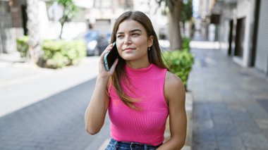 Güneş ışığında ışıldayan, genç ve güzel İspanyol bir kadın kendine güvenir, neşeli gülüşü, akıllı telefonuyla eğlenceli, canlı bir sokak sohbeti yaparken mutluluk saçar..