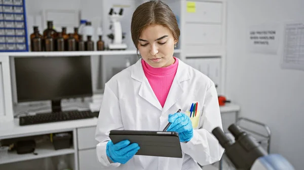 Busy day at the lab, beautiful young hispanic woman scientist seriously engrossed in work, jotting down groundbreaking research on her touchpad.