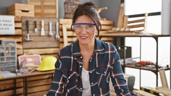 一个戴着安全玻璃的微笑的女人站在一个精心组织的木工车间里 四周都是工具 — 图库照片