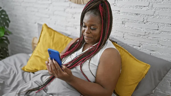 非洲裔美国妇女坐在卧室的床上用智能手机 — 图库照片