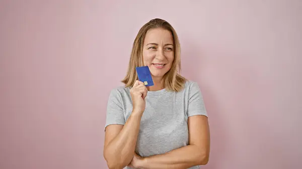快乐的金发女青年自信地拿着信用卡 在孤立的粉色背景上散发出喜悦和财务自信 — 图库照片