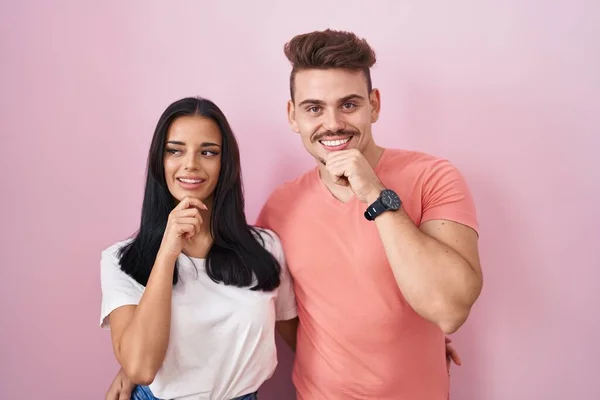 Young Hispanic Couple Standing Pink Background Hand Chin Thinking Question —  Fotos de Stock