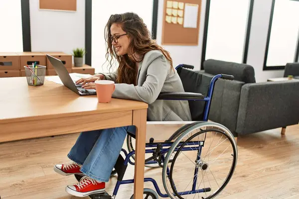 オフィスで車椅子に座ってノートパソコンを使用して若い美しいヒスパニック系女性のビジネスワーカー — ストック写真