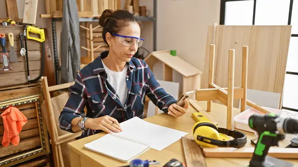 Middle Aged Woman Examines Cellphone Woodworking Workshop Surrounded Tools Safety — Stock Photo, Image