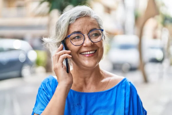 Middle age grey-haired woman smiling confident talking on the smartphone at street