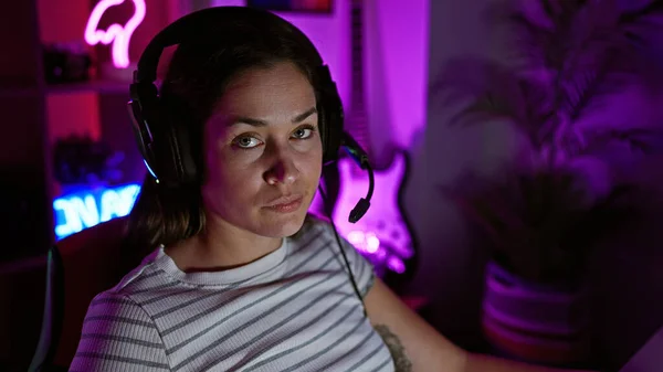 Young woman with headphones in a gaming room at night illuminated by neon light