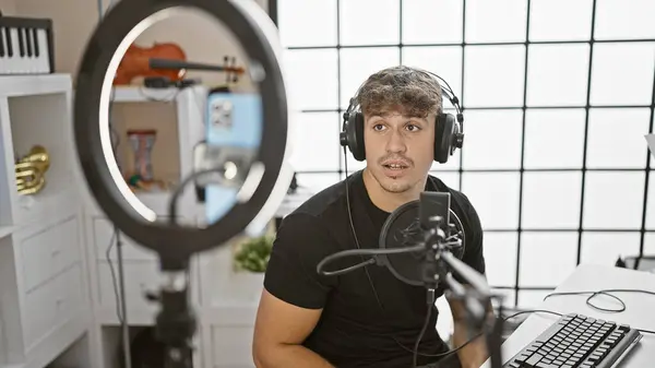 Live on air, young, handsome hispanic man, full of smiles as a professional reporter, commanding the radio show stage. presenting with smartphone indoors at a cosy radio studio.