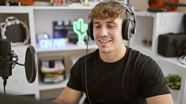 Handsome young hispanic man, flashing a charming smile, enjoyably presents live broadcast show on air at the radio studio, wearing headphones and casually speaking into mic