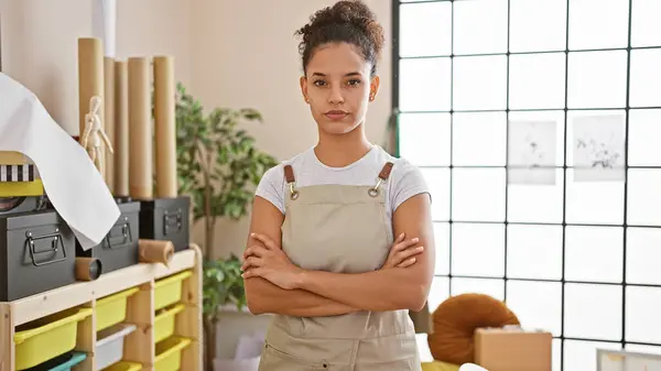 stock image Fiery young hispanic woman, a beautiful artist standing with crossed arms in her cozy art studio, projecting a serious yet relaxed face.