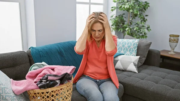 Stressed Middle Aged Woman Sits Couch Laundry Basket Feeling Overwhelmed — Stock Photo, Image