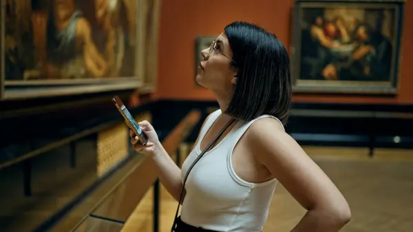 Young beautiful hispanic woman visiting art gallery using smartphone at Art Museum in Vienna