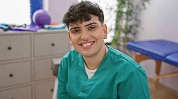 Young man in scrubs smiling in a well-equipped rehab clinic interior capturing healthcare and professionalism.