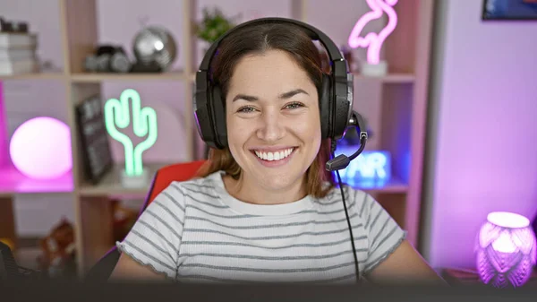 一个戴着耳机 面带微笑的女人 晚上坐在一个有霓虹灯的五彩缤纷的游戏室里 — 图库照片