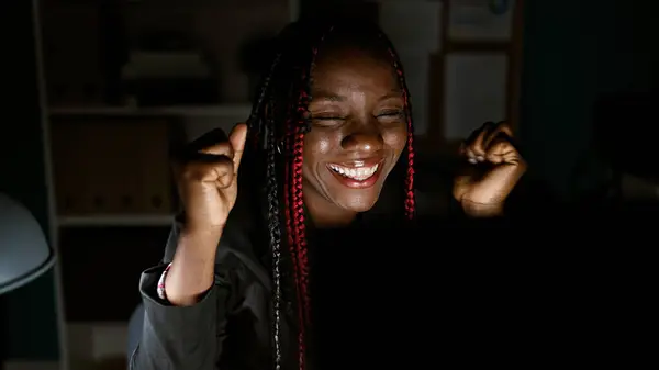 彼女のビジネスの成功を祝うブレードを持つ自信を持ったアフリカ系アメリカ人女性ボスは 夜に照らされた美しいオフィスルームでコンピュータで作業しながら — ストック写真