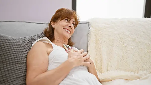 一位面带微笑的中年妇女躺在舒适的家室内灰色的沙发上 流露出一种放松的感觉 — 图库照片