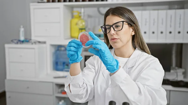 A young woman scientist examines a petri dish with a specimen in a modern laboratory setting.