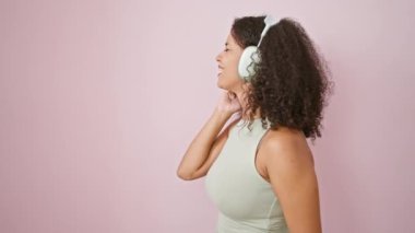 Genç, güzel İspanyol kadın müzik dinliyor ve pembe arka planda dans ediyor.