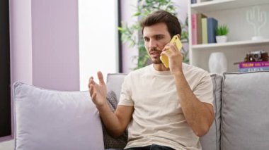 Modern bir apartman dairesinde sakallı genç bir İspanyol telefonda konuşuyor.