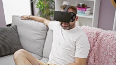 Sanal gerçeklik kulaklığı takan sakallı adam evdeki koltukta oturmuş heyecanını dile getiriyor.