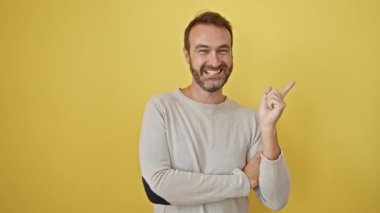 Neşeli orta yaşlı İspanyol bir adam güvenli bir şekilde yan tarafı işaret ediyor ve eğlenceli bir reklam için sarı izole edilmiş bir arka plana karşı dururken açık ağızlı bir gülümseme ile ürünü sunuyor..