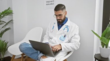 Beyaz laboratuvar önlüklü sakallı bir adam modern bir klinikte bilgisayarla çalışıyor..