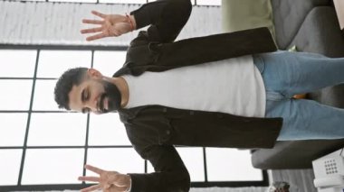 Işıldayan genç adam, kendinden emin bir şekilde yukarı doğru sekiz işareti ile oturma odasından neşe saçar.