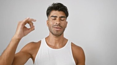 Beyaz kolsuz tişörtlü kendine güvenen bir İspanyol beyaz arka planda, erkeklik ve çekicilik sergiliyor..