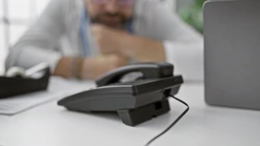 Gri saçlı, olgun bir adam klinikte otururken, bulanık bir telefon önplanıyla kafa yoruyor.