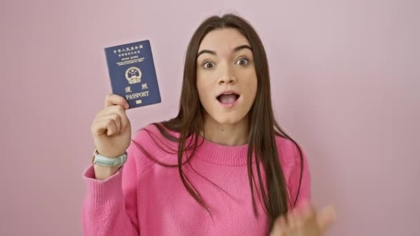 若いヒスパニック系女性は驚きに驚き 手で口を覆った ピンクの孤立した背景上の香港のパスポートをブランディング スナップを始めることを恐れて — ストック動画