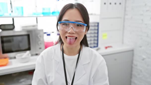 若い中国の科学者少女が研究室で喜んで狂っている クレイジー幸せな女性は面白い顔の表情で舌を出します — ストック動画