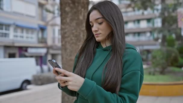 Молодая Латиноамериканка Брюнетками Зеленой Толстовке Поглощена Своим Смартфоном Городской Улице — стоковое видео