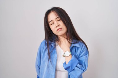 Beyaz arka planda duran genç Çinli kadın ağrılı boyuna dokunuyor, grip, mantar ve enfeksiyon yüzünden boğazı ağrıyor. 