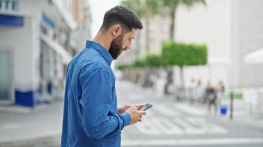 Genç İspanyol adam akıllı telefon kullanıyor. Sokakta ciddi bir ifadesi var.