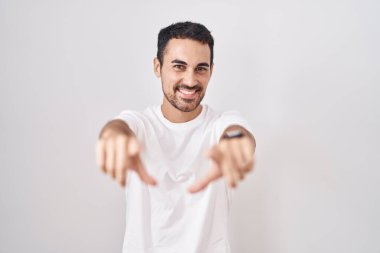 Beyaz arka planda duran yakışıklı İspanyol adam seni ve kamerayı işaret ediyor, pozitif ve neşeli gülümsüyor. 
