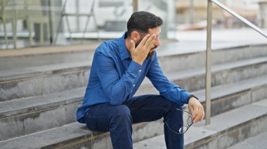 Genç İspanyol iş adamı merdivenlerde oturuyor. Sokakta gözlük çıkartıyor.