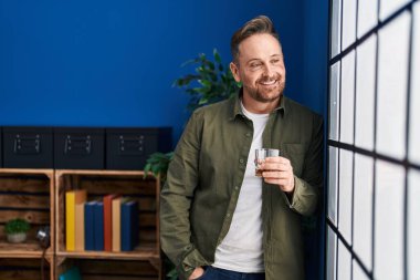 Genç beyaz adam evde dikilip bir bardak viski içiyor.