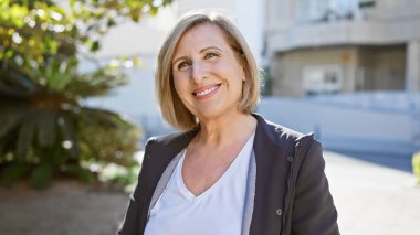 Güneşli bir şehir sokağında gülümseyen kendinden emin orta yaşlı bir kadın..