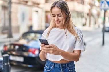 Sokakta akıllı telefon kullanan, kendine güvenen genç sarışın kadın.