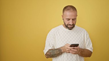 Yakışıklı genç adam, akıllı telefon teknolojisi kullanan, parlak sarı arka planda izole edilmiş, ciddi bir metin konuşmasına dalmış..