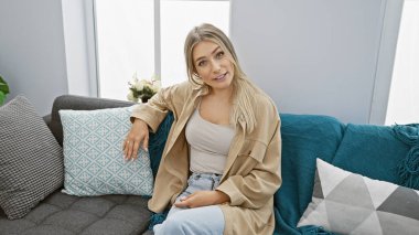 Evdeki koltukta oturan neşeli, genç sarışın kadın, ışıl ışıl gülüyor ve kendine güveni tamdı.