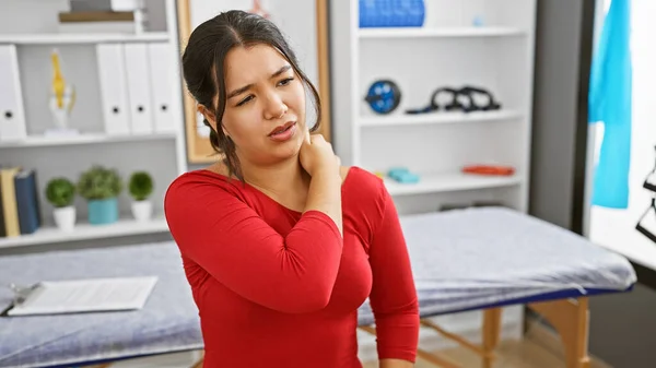 Hispanic Woman Feeling Neck Pain Modern Clinic Room Showcasing Healthcare — Stock Photo, Image