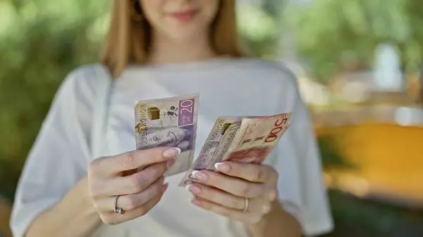 Young blonde woman counting swedish krone banknotes at park
