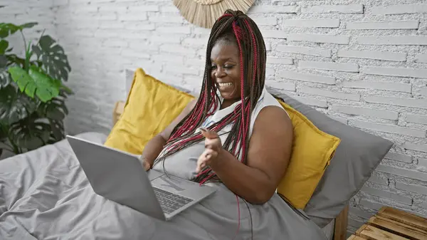 African american woman doing video call with laptop sitting on the bed at bedroom